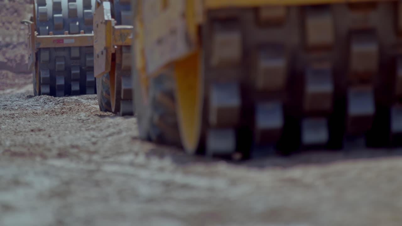 Industrial sheep foot rollers use vibrating drums to compact dirt on a construction site
