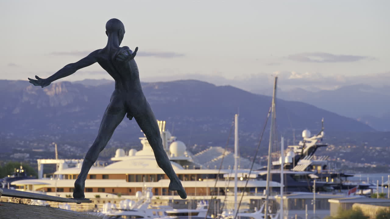 Antibes, France - June 8, 2025: Bronze sculpture "Grand Defi" by Nicolas Lavarenne with boats docked in the background