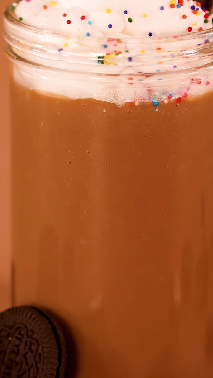 Lenta panoramica verso il basso di un cremoso milkshake al cioccolato con panna montata, codette colorate, biscotti e cioccolato.