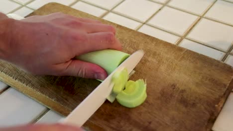 Cutting-a-leek-on-wooden-board,-100%-speed