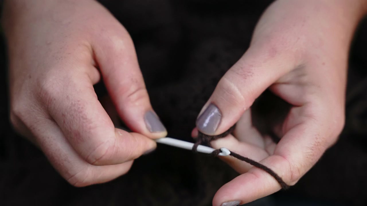 Donna che lavora all'uncinetto con filato e uncinetto, primo piano delle mani che creano un punto.
