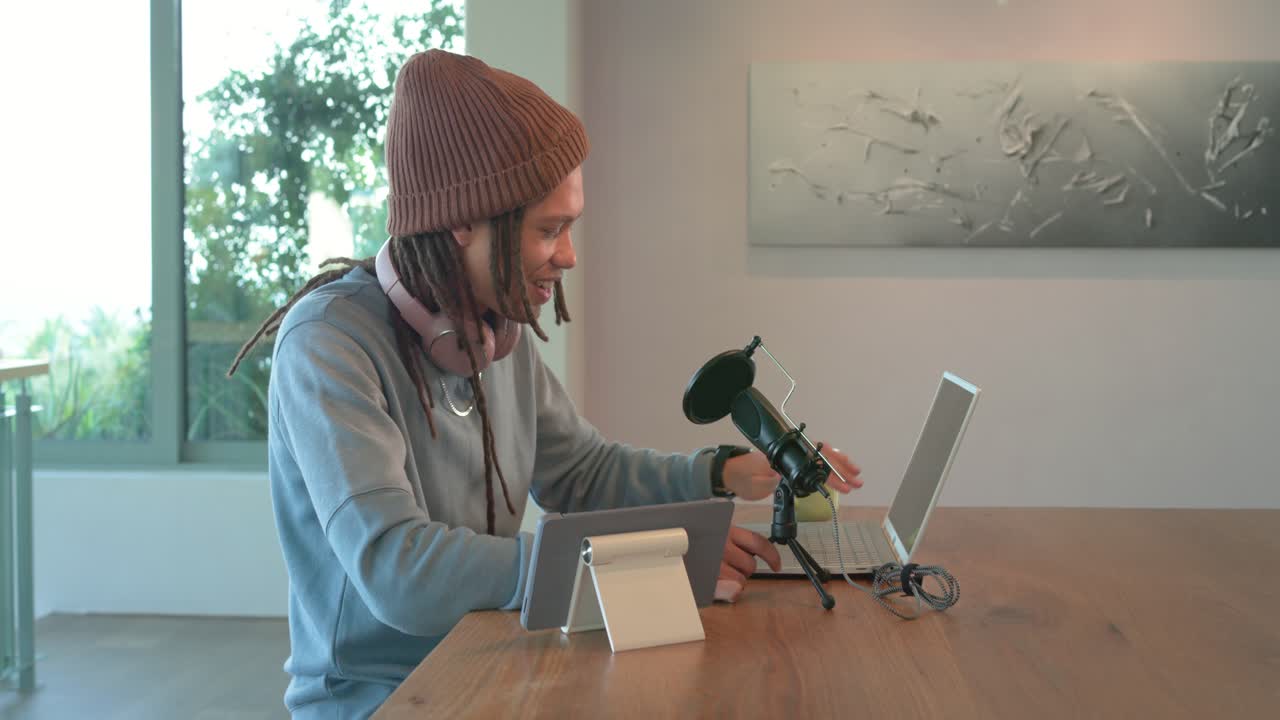 Un podcaster uomo di mezza età entra nell'inquadratura, tocca il tablet, regola il microfono e fa un podcast al bancone.