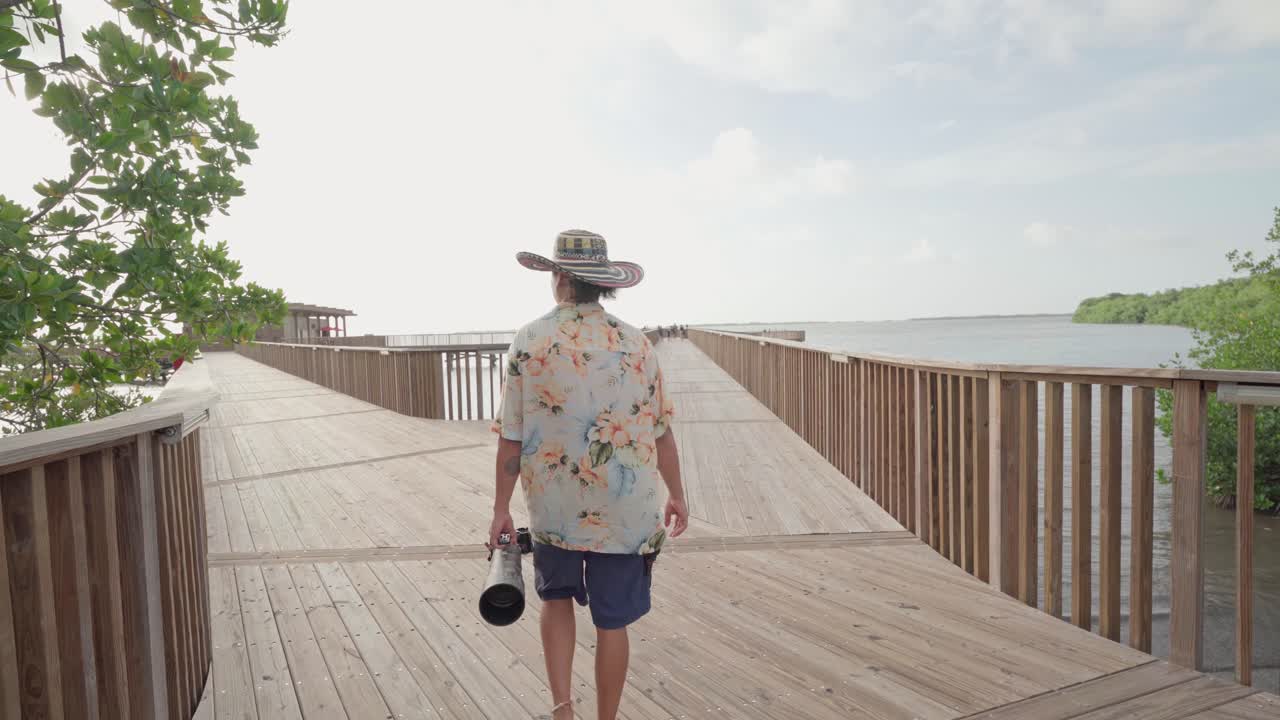 Tourist with a camera walking on a wooden path over the water at a natural reserve, cienaga de mallorquin, barranquilla