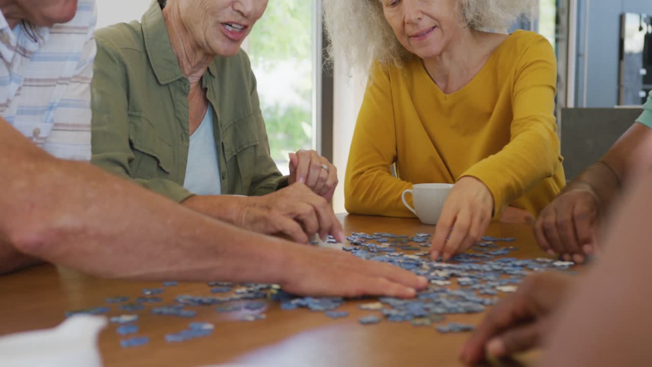personas mayores felices y diversas jugando rompecabezas en la mesa en el hogar de ancianos