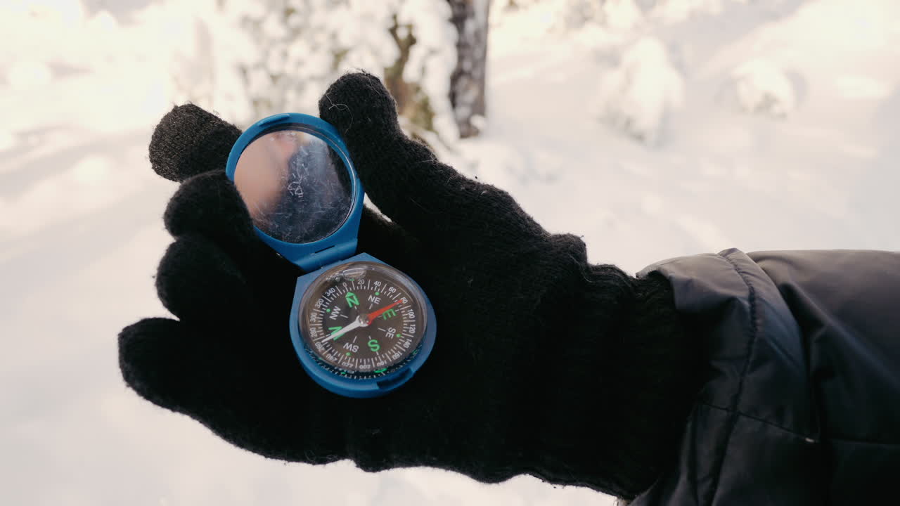 Hand holding a compass in snowy landscape