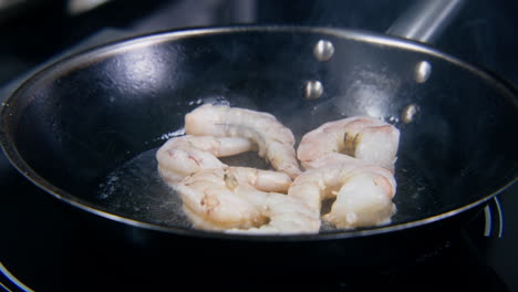 male cook puts shrimp in frying pan with cooking oil sprinkles salt the chef cooks delicious dish