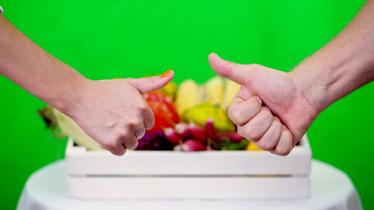close-up, Two hands showing thumbs up sign, Ok sign, against Chromakey, green background and a box full of different vegetables, in studio. concept of crop counting, harvest of vegetables