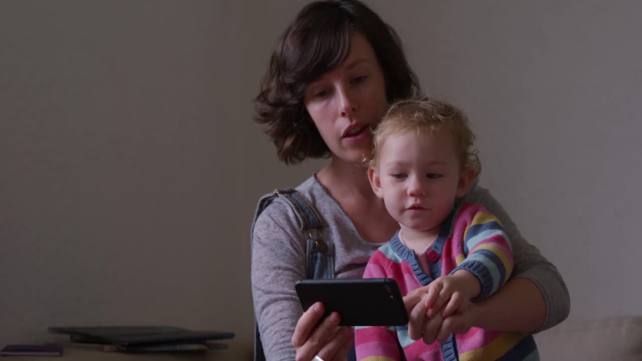 Caucasian woman with baby looking smartphone at home