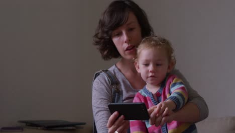 Caucasian-woman-with-baby-looking-smartphone-at-home