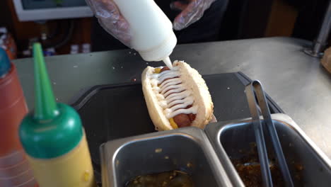 poniendo mayonesa en un sándwich de perrito caliente con ketchup y mostaza