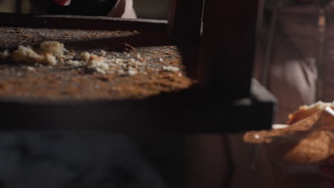 close-up of individual in winter clothing holding crispy snack while dropping small feed pieces for birds, blurred hand movement with warm lighting