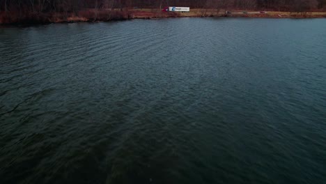 epic-aerial-reveal-of-a-red-semi-truck-and-white-trailer-parked-on-side-of-a-lake