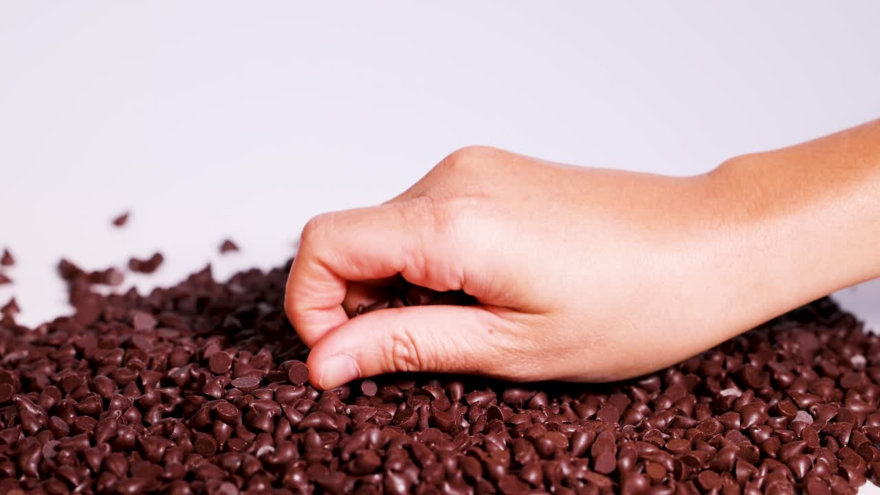 Hands interact with chocolate pieces on a white surface under bright lighting, creating a tactile and engaging visual experience