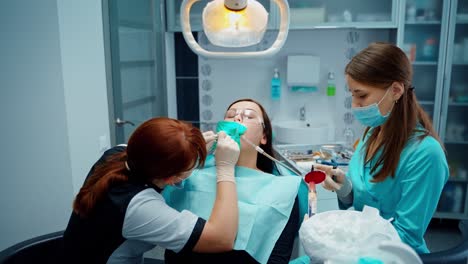 female dentist treating teeth to female patient. woman sitting with open mouth at dentistry. medical staff working in modern stomatology clinic.