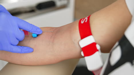 nurse in sterile gloves taking vein blood. doctor pricks needle into patient's arm in hospital laboratory. blood sampling for corona virus antibodies. close-up.