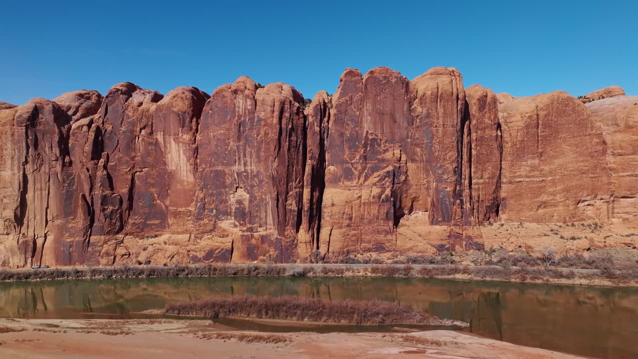 Drone strong midday light over Moab steep sheer cliff walls, illuminating red sandstone formations
