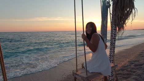 young and carefree girl, looking and smiling at camera while swinging next to ocean