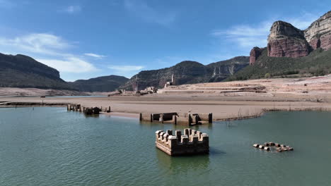 Aerial-view-approaching-submerged-abandoned-building-remains-under-Sau-reservoir-water-in-Catalonia-rocky-mountain-valley