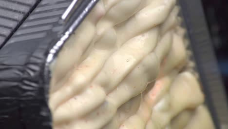 Dutch-angle-view-of-delicious-and-tasty-chicken-mentai-cheese-surface-cooking-with-hot-burning-torch-flame-of-fire-sizzling-food-in-silver-foil-take-out-pan,-static-extreme-close-up