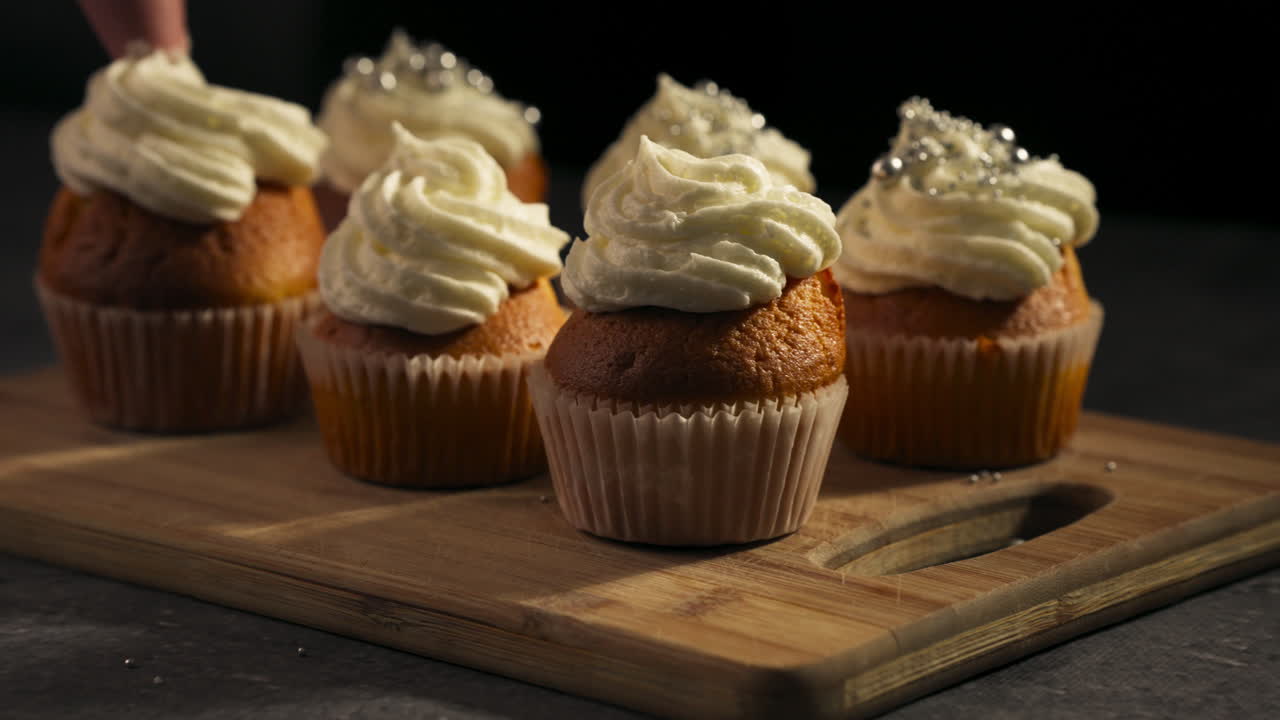 Primo piano di ciuffi di glassa cremosa sui cupcake per una splendida finitura del dessert e codette colorate in cima, carrello a sinistra in slow motion