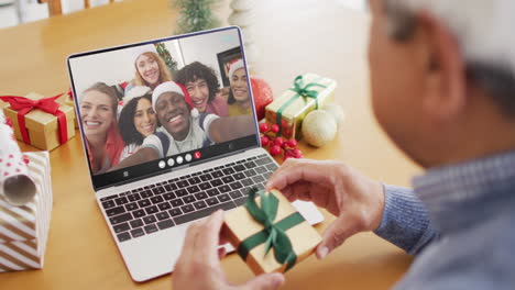 biracial man with gift having laptop video call with happy diverse friends