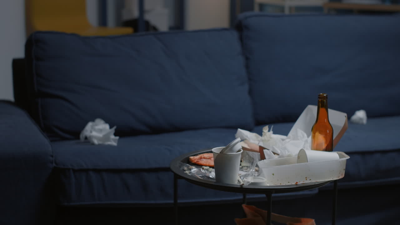 Chaos in empty living room with food leftover and bottle of beer on table