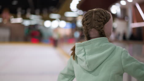 close-up of a lady skating on an ice rink, wearing a mint green hoodie and a pink headband with her hair in braids