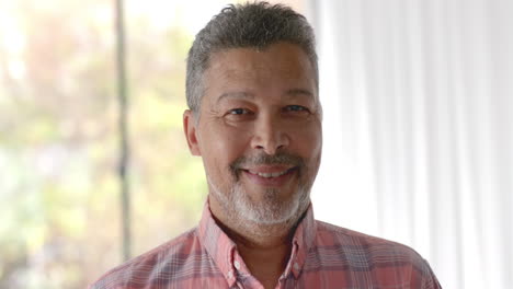 Portrait-of-happy-senior-biracial-man-smiling-in-sunny-room-at-home,-slow-motion