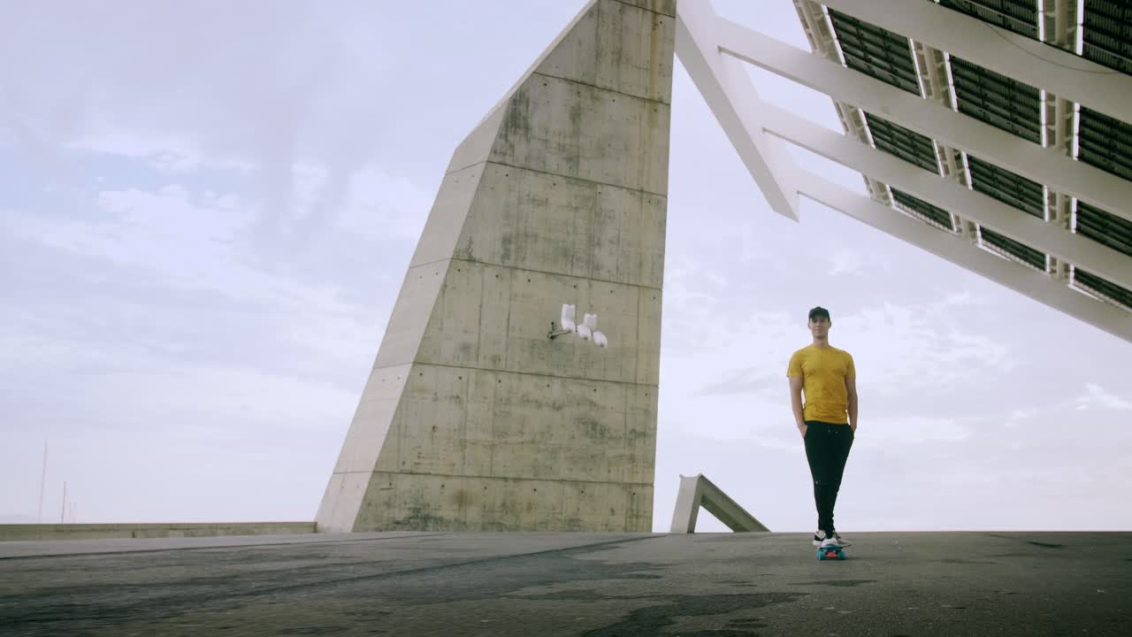 joven y atractivo hombre de moda patinando rápido bajo un panel solar en un día soleado por la mañana con un fondo urbano en cámara lenta