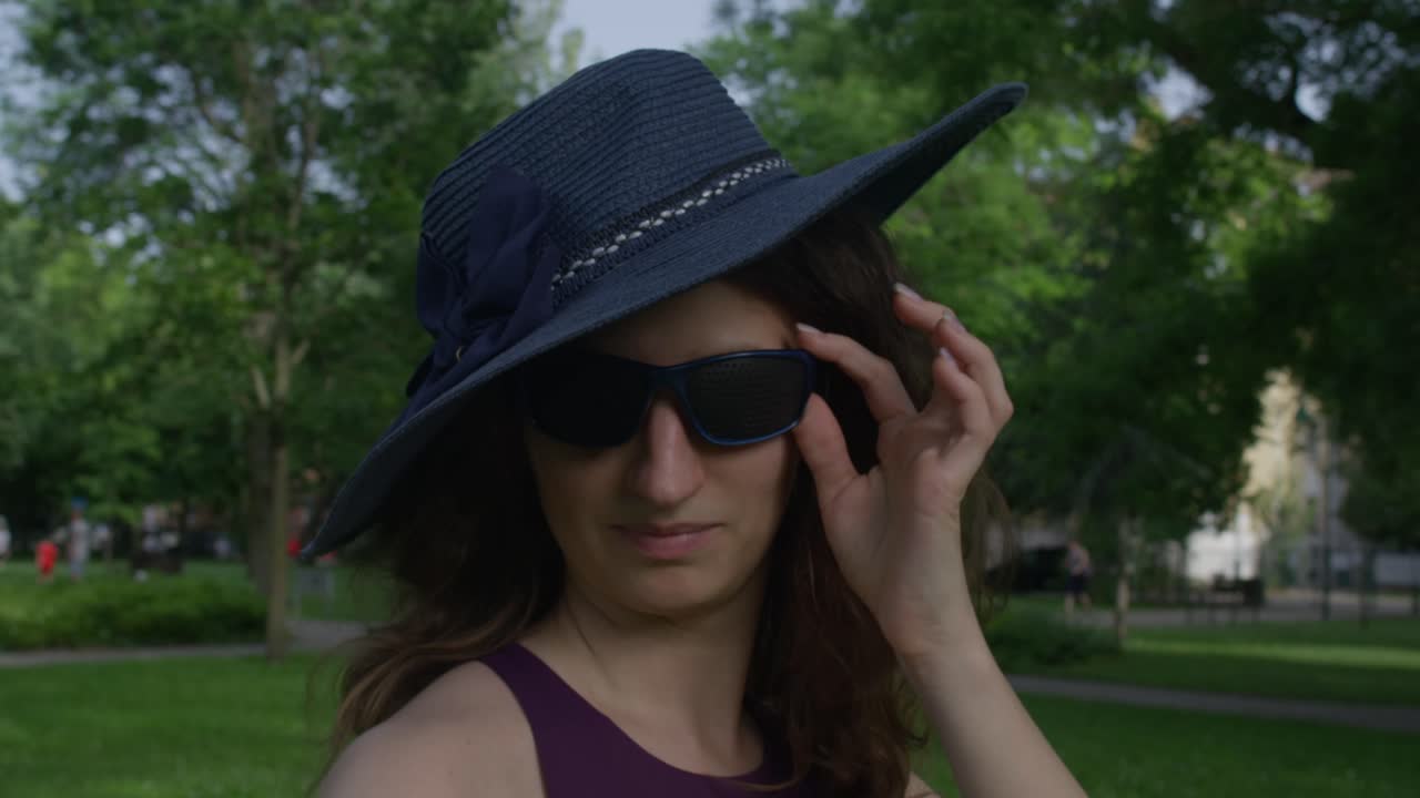 красивая леди с голубой шляпой и очками снимает очки, чтобы видеть невооруженным глазом.