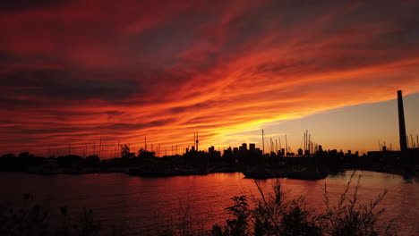 as night creeps in, moody red clouds linger like a blanket over the boat marina and city skyline