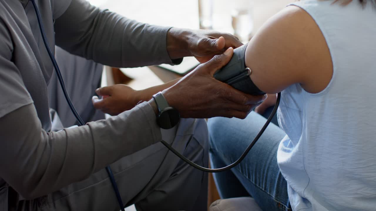 African American clinician placing blood pressure cuff on mature patient's upper arm for reading