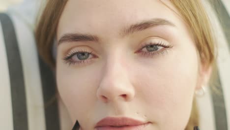 Close-up-view-of-beautiful-blue-eyed-young-woman-slowly-taking-off-her-sunglasses-and-looking-to-the-camera-with-bewitching-look