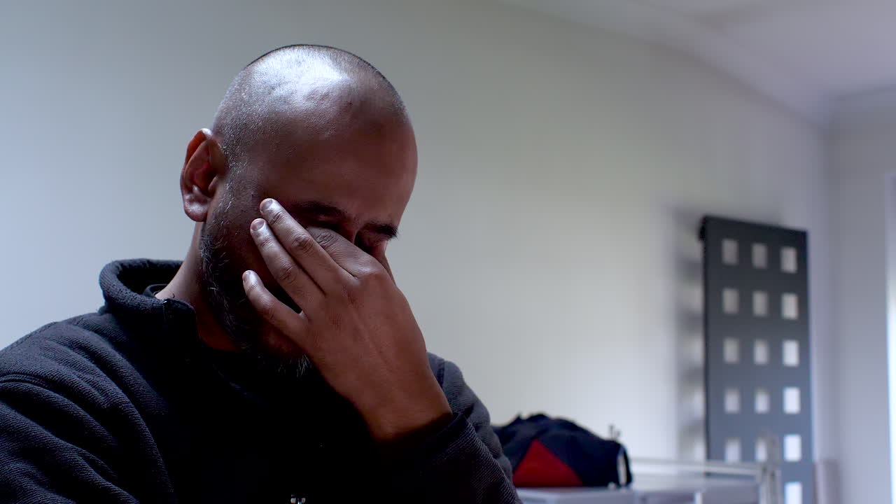 Man in a dark shirt feeling stressed with his hand on his forehead in an office setting, shallow focus