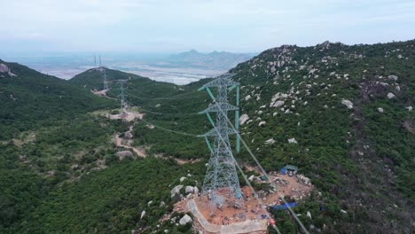 aerial drone footage of high voltage power transmission towers with line pylon in mountainous area to distribute electricity - natural landscape and industrial concept for sustainable development