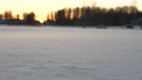 Suelo-Cubierto-De-Nieve-Mientras-El-Fuerte-Viento-Sopla-Nieve-Y-Puesta-De-Sol-En-Segundo-Plano