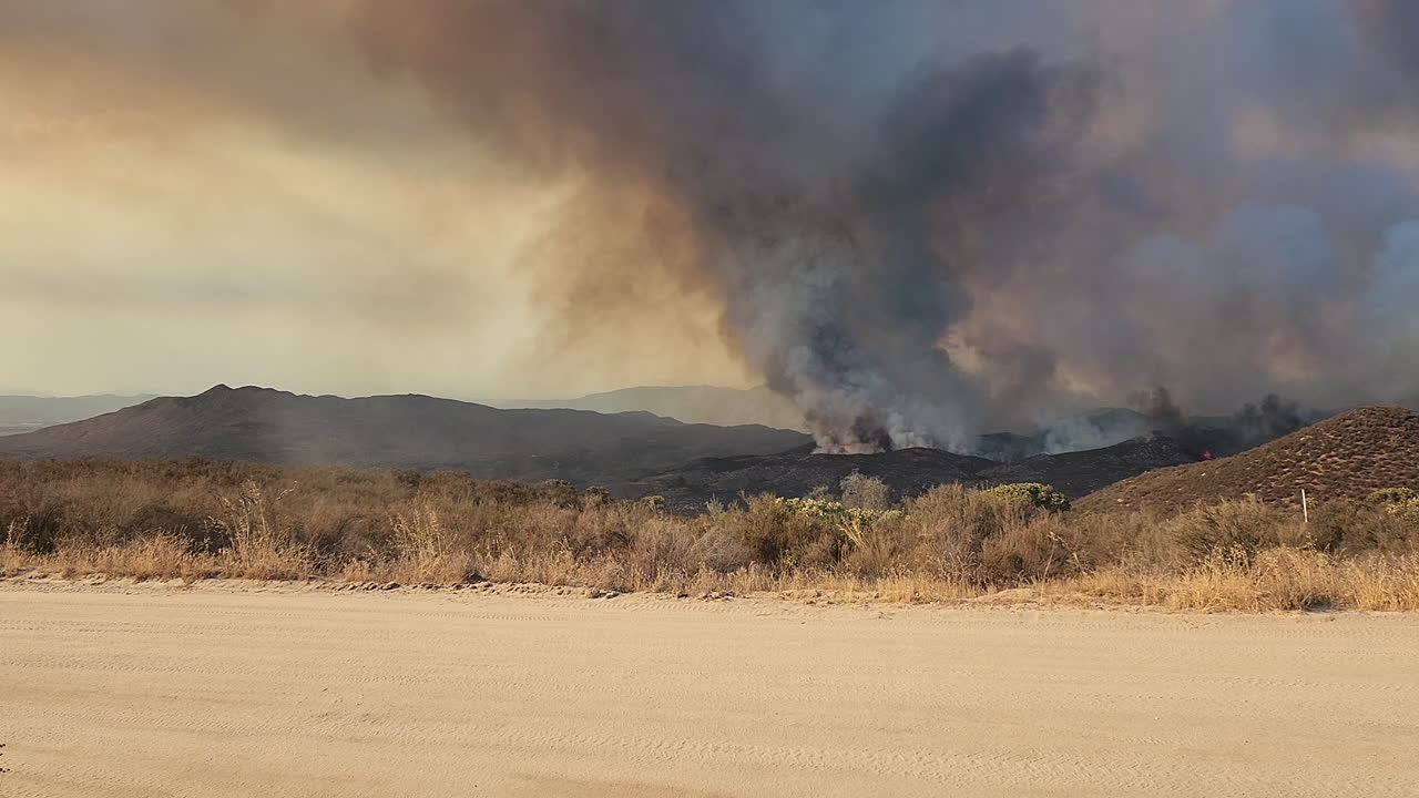 coche rojo conduciendo en el camino de tierra con vistas al humo oscuro que se eleva en el cielo durante el incendio de fairview en california, ee.uu.