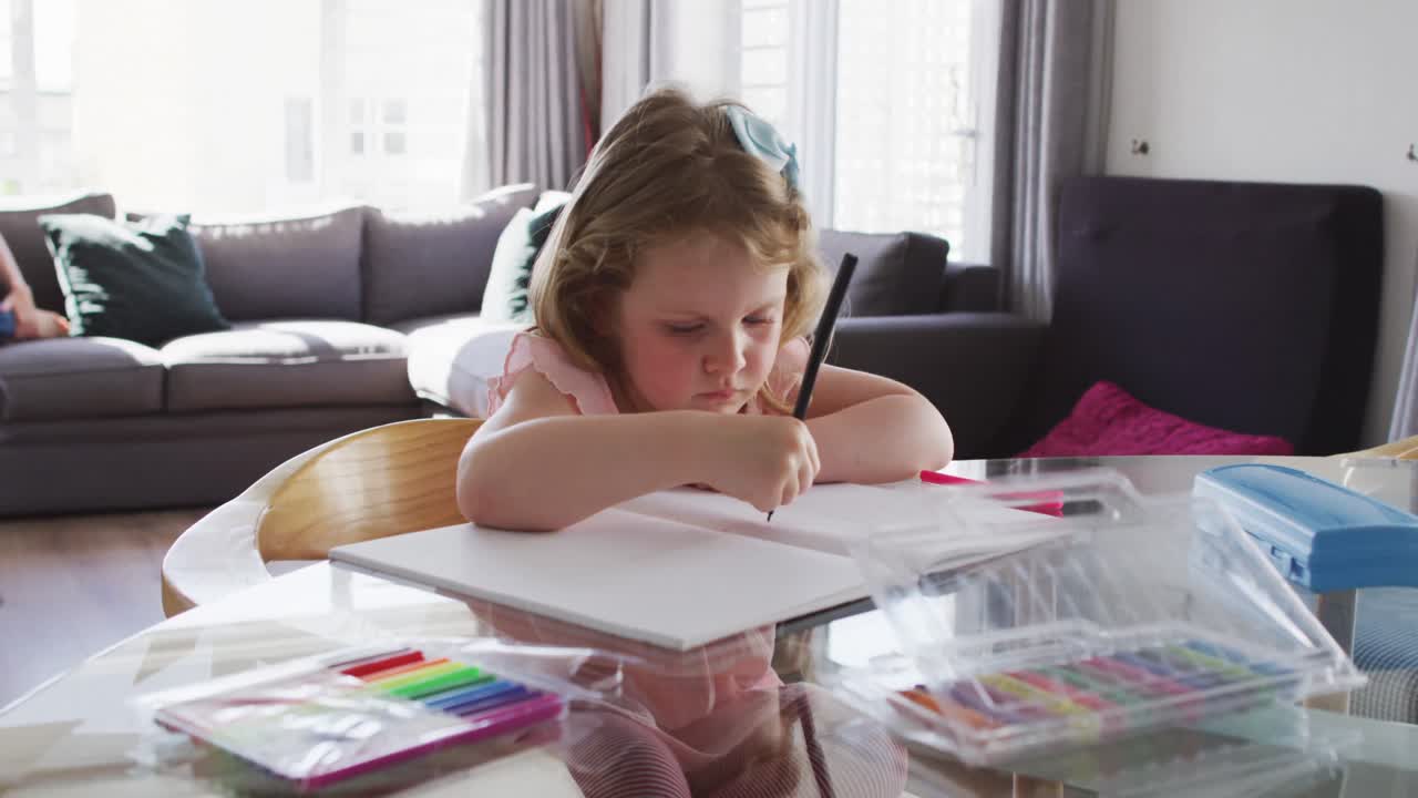 Bambina caucasica che disegna su un quaderno in soggiorno