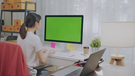 pequeña empresa de puesta en marcha, joven mujer asiática comprobando el pedido en línea en la computadora con pantalla verde. y embalaje de cajas para productos para enviar a los clientes.