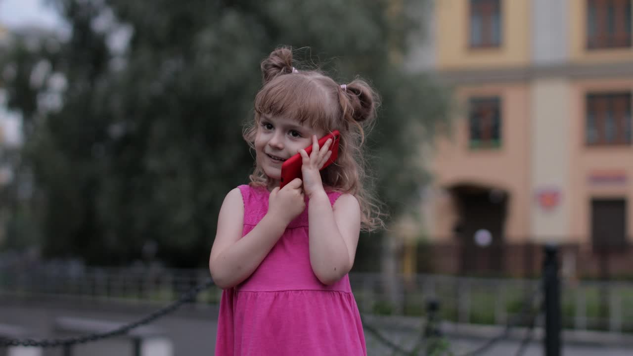 niña hablando por teléfono inteligente al aire libre. niño con vestido rosa hablando por teléfono móvil en la calle de la ciudad