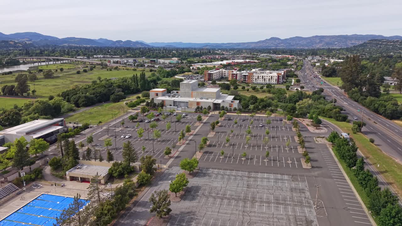 Ampio parcheggio, per lo più vuoto, al Napa Valley College in California, ripreso da una prospettiva aerea con drone che mostra il paesaggio circostante, le montagne e l'autostrada vicina in una giornata nuvolosa