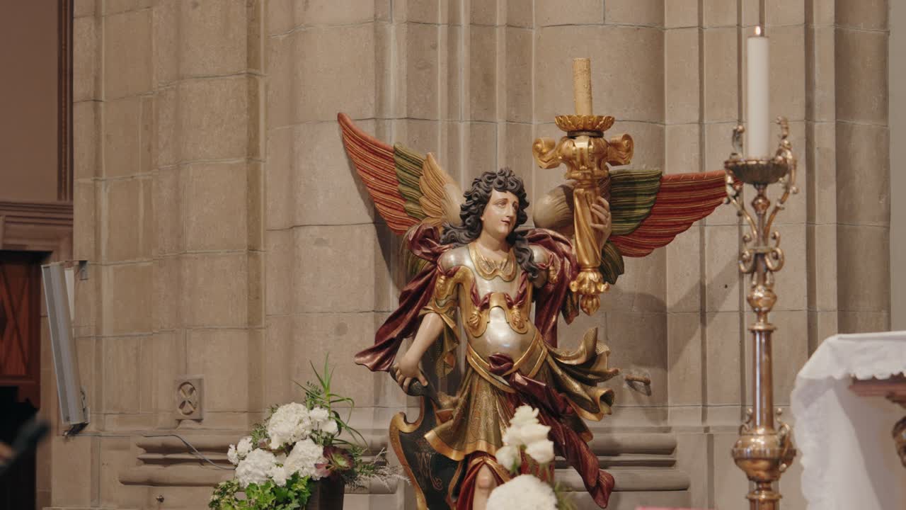 baroque style angel statue with colorful wings holds candle in richly decorated church altar