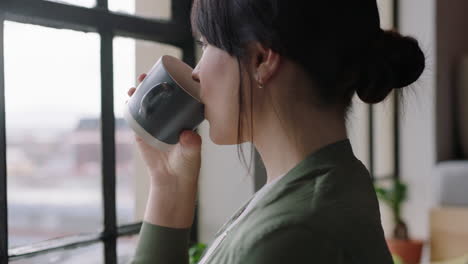 beautiful young woman drinking coffee at home enjoying relaxed morning looking out window thinking planning ahead in cozy apartment loft