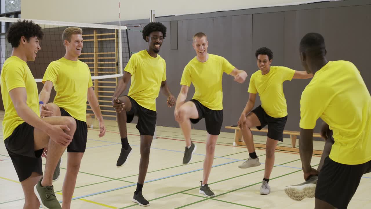 Six male players in yellow tops black shorts following leader's kick, warming in gym near net