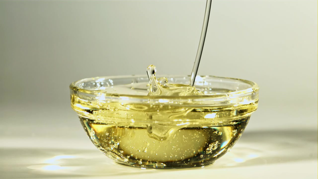 ガラスのボウルに黄金色の食用油がスローモーションで注がれる様子