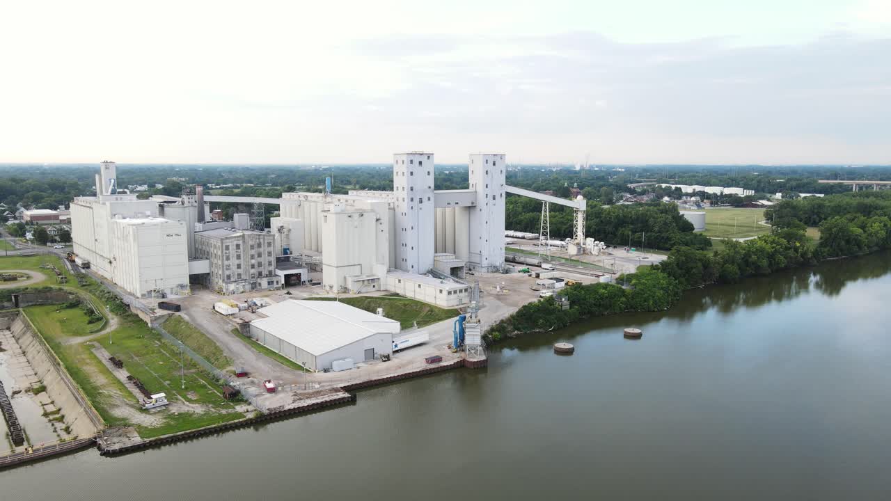 Panoramica aerea di un grande impianto di silos per cereali e deposito alimentare sulla riva di un fiume con un molo per consentire alle navi di caricare e scaricare