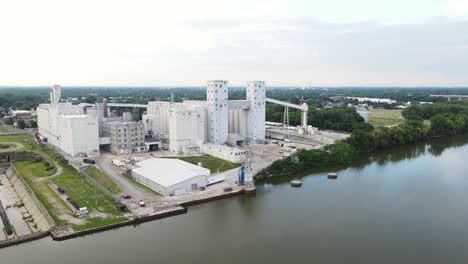 toma panorámica aérea de un gran elevador de granos y una instalación de almacenamiento de alimentos en la orilla de un río con un muelle para permitir que los barcos carguen y descarguen