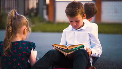 little girl with pencil talks to boy reading book on street