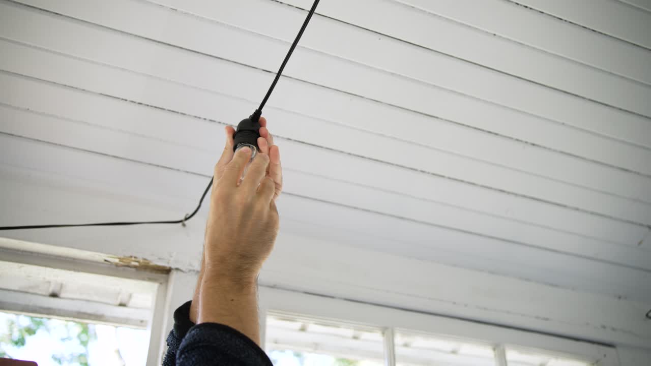Uomo bianco che sostituisce una lampadina pendente in veranda