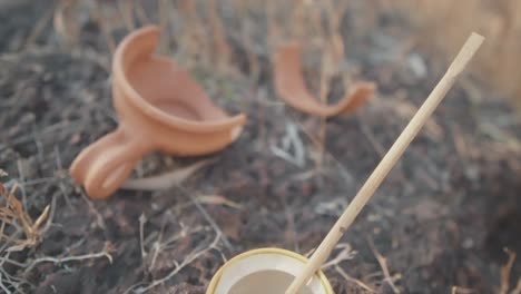 brown clay pot on the ground broken in half near a white and yellow bowel with white glue